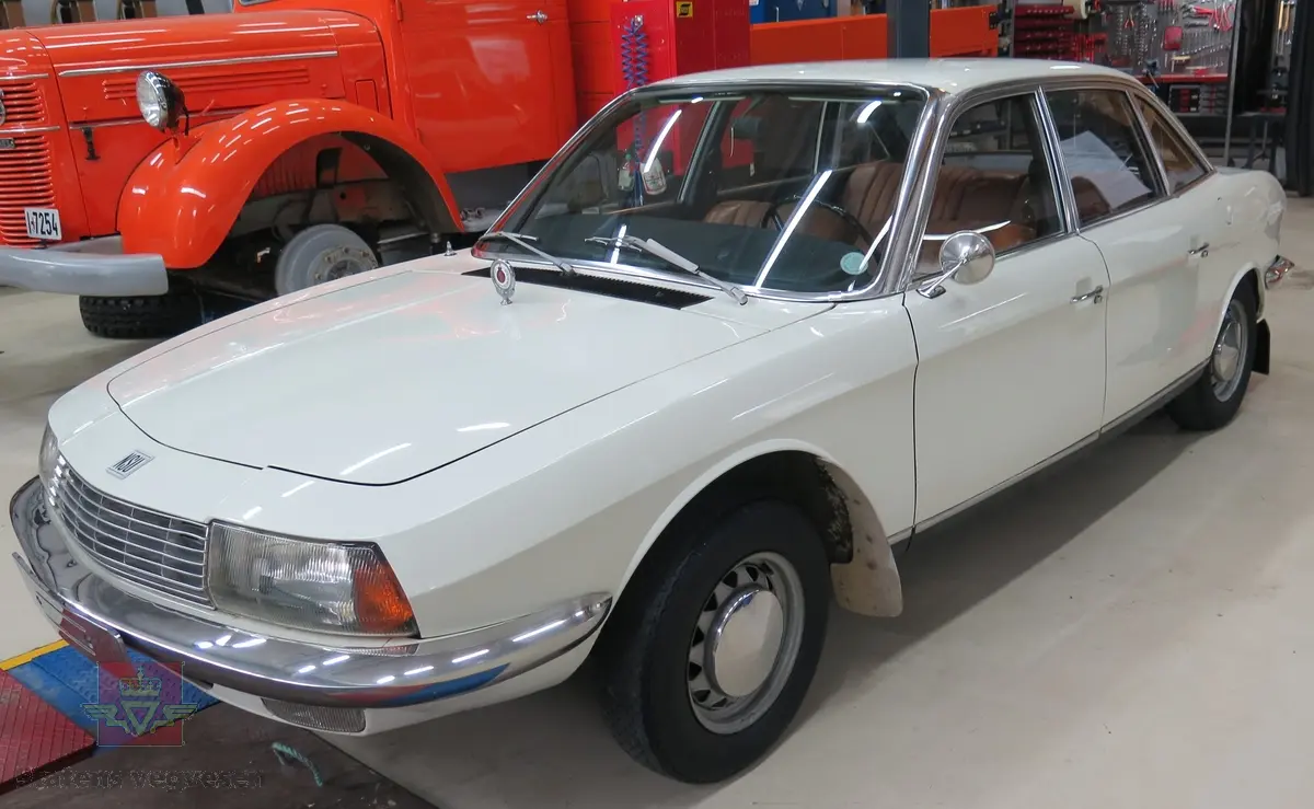 NSU RO 80. 4-dørs hvit bil med brunt interiør. Bilen har en bensindrevet dobbel NSU/Wankel rotasjonsstempelmotor, med sylindervolum på 994 kubikkcentimeter (cm3), og effekt på 115 DIN HK. Dekkdimensjon foran og bak skal standard være 175 HR 14. Framhjulstrekk. Girkasse med 3 gir framover pluss revers. Kilometerstand er 75385.