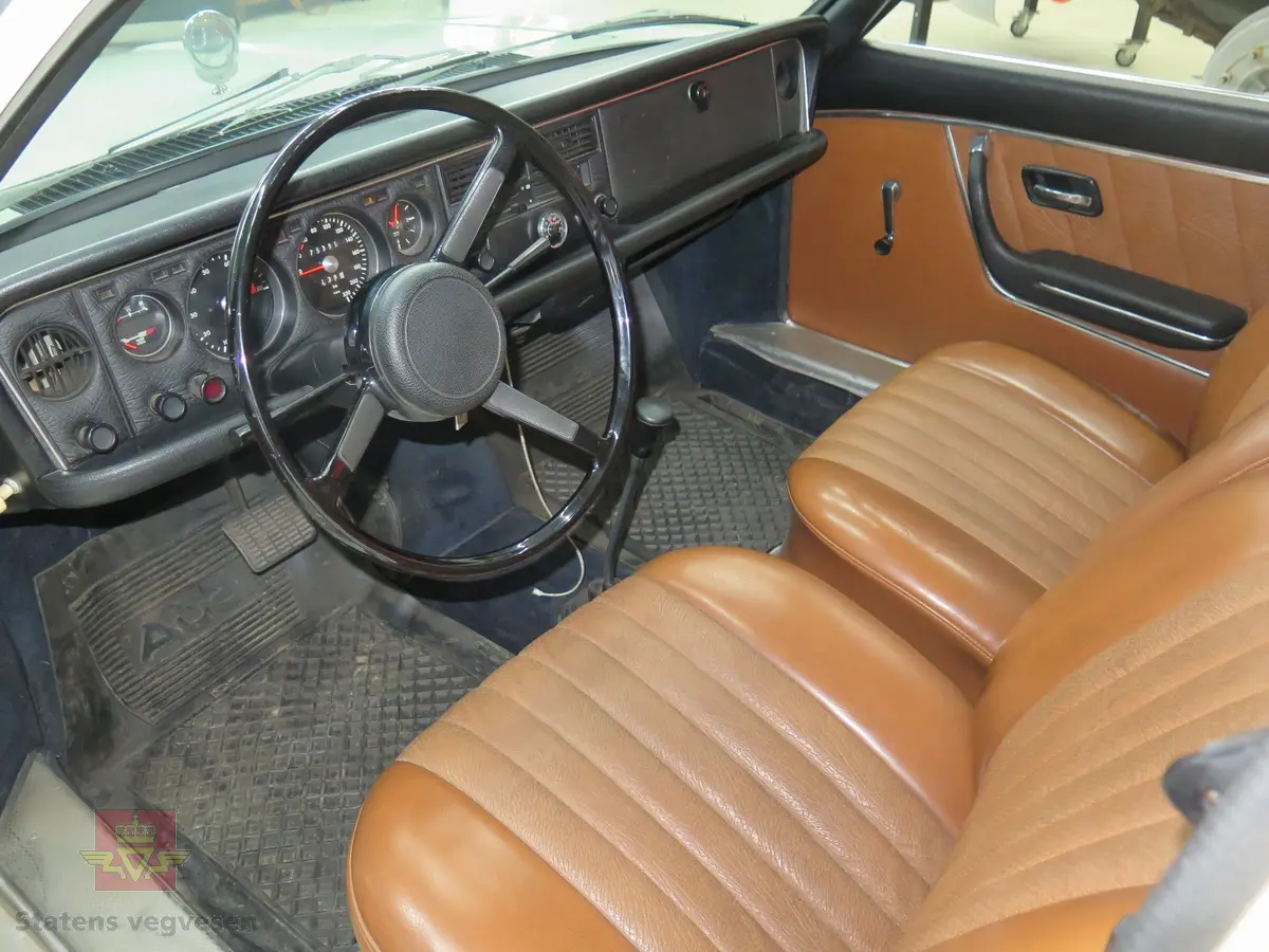 NSU RO 80. 4-dørs hvit bil med brunt interiør. Bilen har en bensindrevet dobbel NSU/Wankel rotasjonsstempelmotor, med sylindervolum på 994 kubikkcentimeter (cm3), og effekt på 115 DIN HK. Dekkdimensjon foran og bak skal standard være 175 HR 14. Framhjulstrekk. Girkasse med 3 gir framover pluss revers. Kilometerstand er 75385.