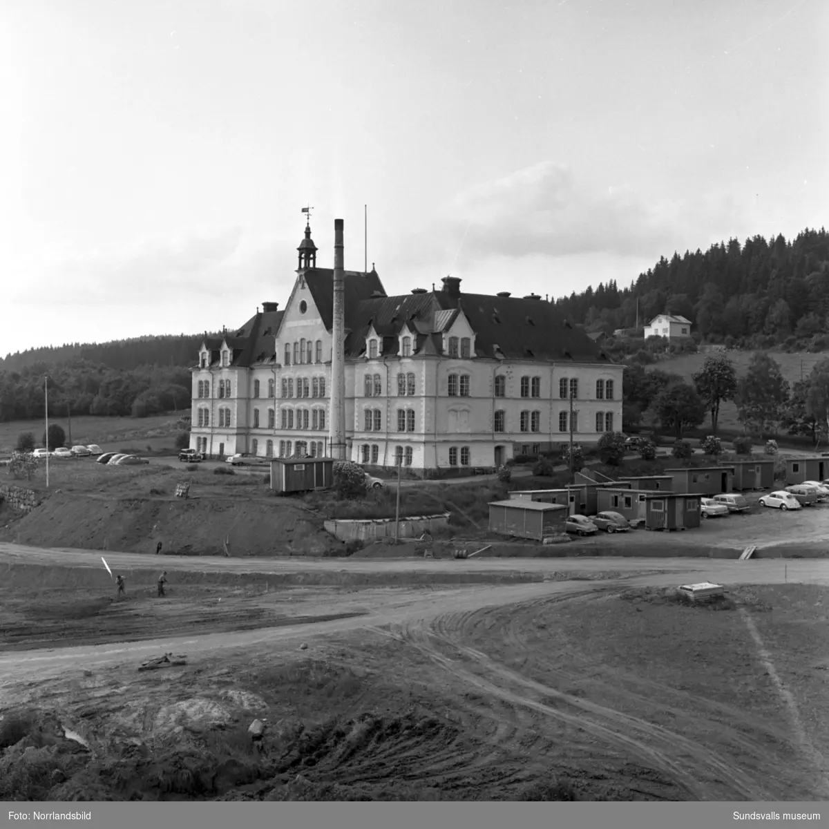 Exteriörbilder av Birstahemmet, Sköns försörjningshem, ett par år innan det rivs. I förgrunden pågår markplanering för industriområdets utbredning.