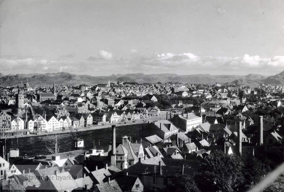 Valbergtårnet og Petrikirken til venstre. Hetlandskirken midt i bildet. Dette fotografiet later ikke til å være et flyfoto...Denne serien med flyfoto fra K. Harstad, har kommunen kjøpt av Johan Ottesens Fotoarkiv. ..Karl Harstad, som grunnla K. Harstad kunstforlag (Oslo Prospektkortfabrikk) i 1925, var den første sivile flyfotoprodusenten i Norge. Som postkortprodusent var Harstad opptatt av nhye produkttyper. I 1929 dannet han sammen med andre selskapet FotoFly og kjøpte fly i Tyskland. Selskapet skulle drive både passasjerflyging og fotograferin. I 1929 fotgraferte selskapet de fleste byene langs kysten av Norge, også i Rogaland. Postkortene med flyfotografi ble produsert med navnet Flyfoto, senere med navnet K. Harstad. En annen stor K. Harstad-postkortserie fra Rogaland skriver seg fra flyfotografering 1950-1951. Da fotograferte firmaet både byer og mindre tettsteder og bygder i fylket. Det er uvisst hvor omfattende K. Harstad sin flyfotoproduksjon var i Rogaland før firmaet ble nedlagt ved overgangen til bruk av fargefoto tidlig på 1960-tallet. Så langt man kan se av postkortsamlinger ved kulturverninstitusjonene og hos private, viser de aller fleste kortene byer og tettsteder, ikke enkelteiendommer og bedrifter.