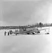 Flygplan B 3 nödlandad på Storsjöns is efter flygning i hårt väder i februari 1946. Skidåkare vid flygplanet. Vy snett bakifrån.