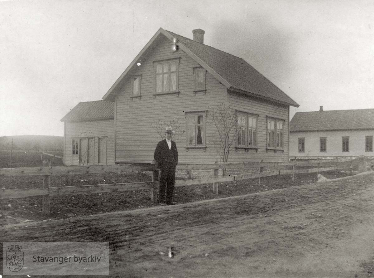 Mann ved veien foran trehus. Muligens på Jæren (evt. Hinna eller Mariero ?)