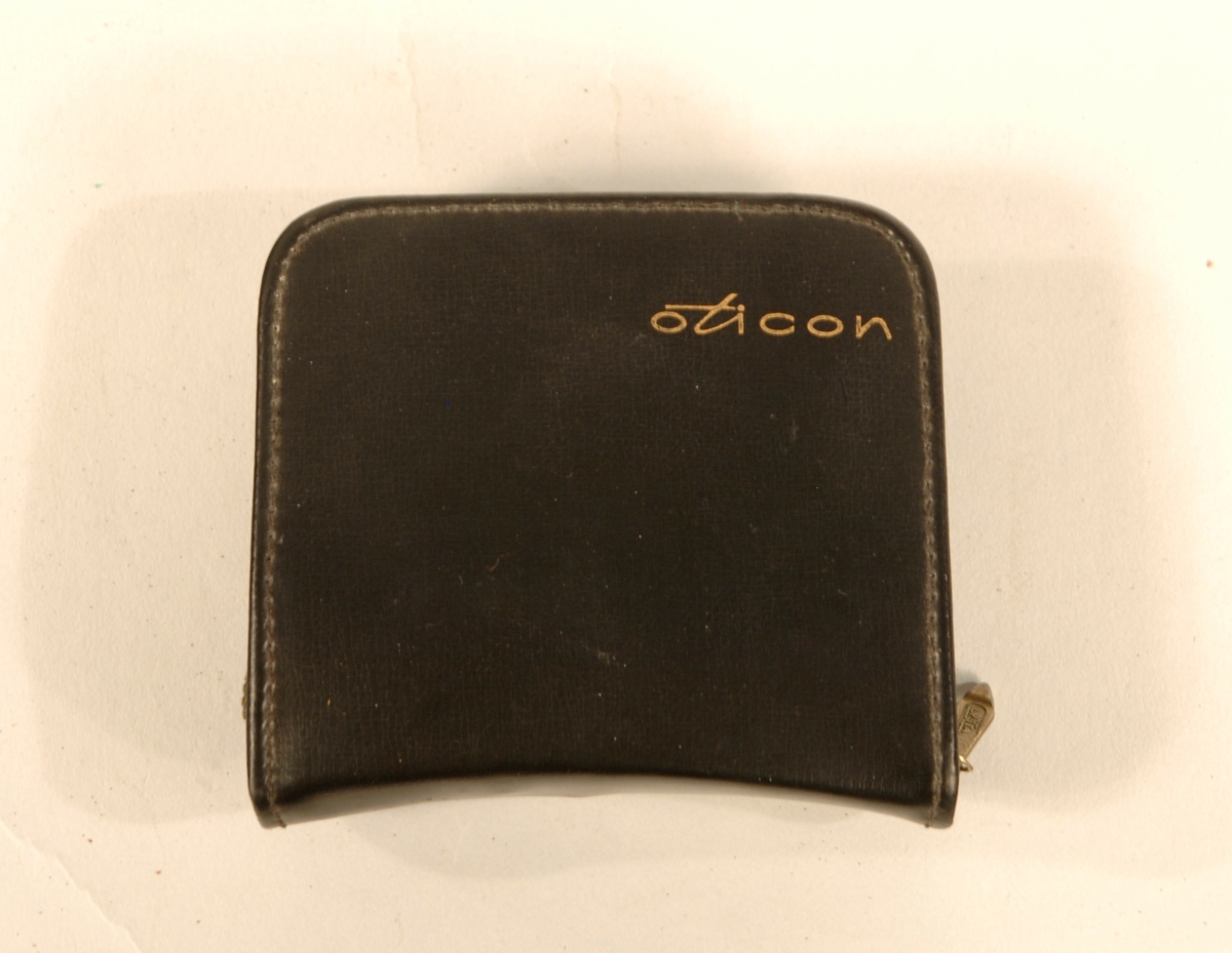 Høreapparat med svart skinnveske med glidelås. Gullfarget batteri beholder, plast apparat. Komplett.