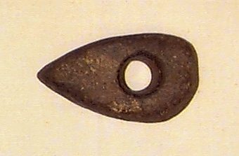 Av finkornig bergart. Delvis slipad. Oregelbundet nackparti. Plan ovan- och undersida, i det närmaste raka sidor.