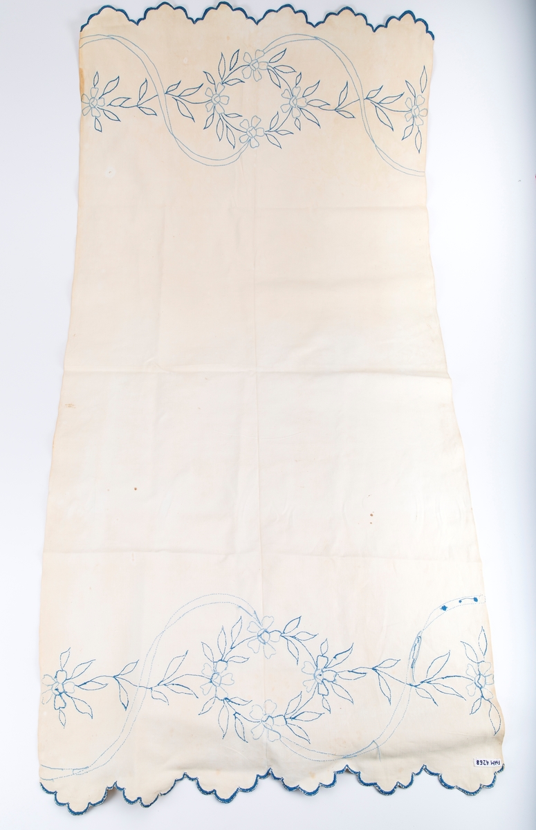 Vevet med blått konturstingsbroderi. Motiv; Blomster og ranker- Blåbroderte tunger i hver ende. Fabrikkert