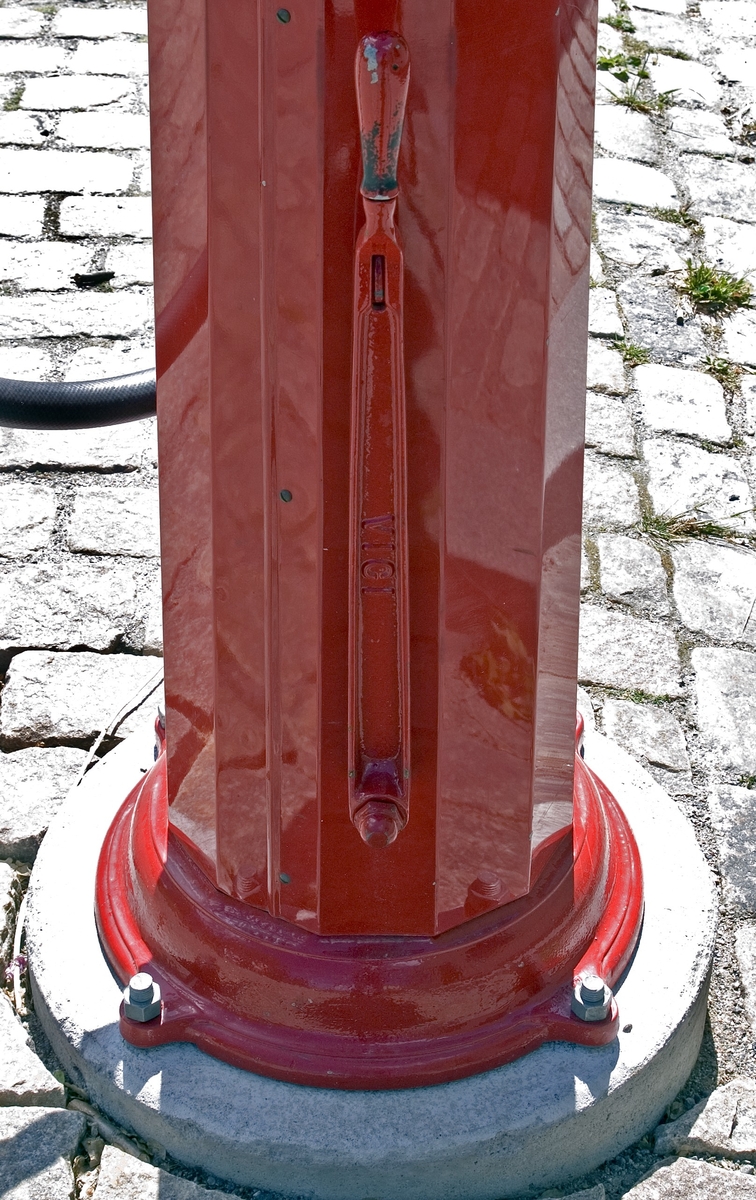 Bensinpump, fabriksgjord. Överst sitter en glasglob, SKAFOR.0015125 på ett metallfäste.  Under globen en cylinder av glas med mätmekanism och gradering. Därunder kommer det rödlackade pumphuset av stål. På en sida sitter en etikett av metall med text: Enligt Kungl. Maj:ts förordning angående eldfarliga oljor är det Förbjudet [understruket] att härstädes Röka Tobak [understruket] samt Tända [understruket] eller Medföra Eld [understruket]. Den som bryter mot sagda föreskrift, äventyrar jämlikt förordningen angående eldfarliga oljor § 60 ansvar av böter från och med 10 t.o.m. 500 kr." Etiketten sitter strax ovanför ett pumphandtag med omgivande dekorativt utformade "bricka" av metall och handtag svarvat av trä. "Brickan" är rund och utformad med graderingar från 0 till 25 med femliters intervaller. Text: PUMP IV-SC 54 A.B. J.C. LJUNGMAN MALMÖ VICI No 6705, ett räkneverk och LITER. Till höger om detta sitter ett annat pumphandtag av rödlackerat stål, fäst nertill. Ovanför etiketten börjar bensinslangen av gummi i ett metallfäste. Den fortsätter i en böj neråt till vänster, runt och upp och avslutas av den utgående kranen av metall, som hänger i ett hål på cylindern. Där bredvid finns också en låsbar lucka.