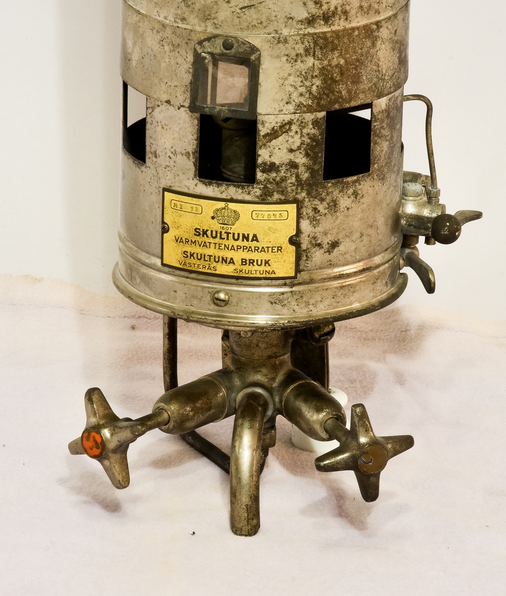 Varmvattenberedare i metall med texten "Har texten " 1607 Skultuna, Varmvattenapparater, Aktiebolaget Svenska Metallverken, Skultuna, Västerås Sverige" på sig, samt två nr: MT 12, 77075.