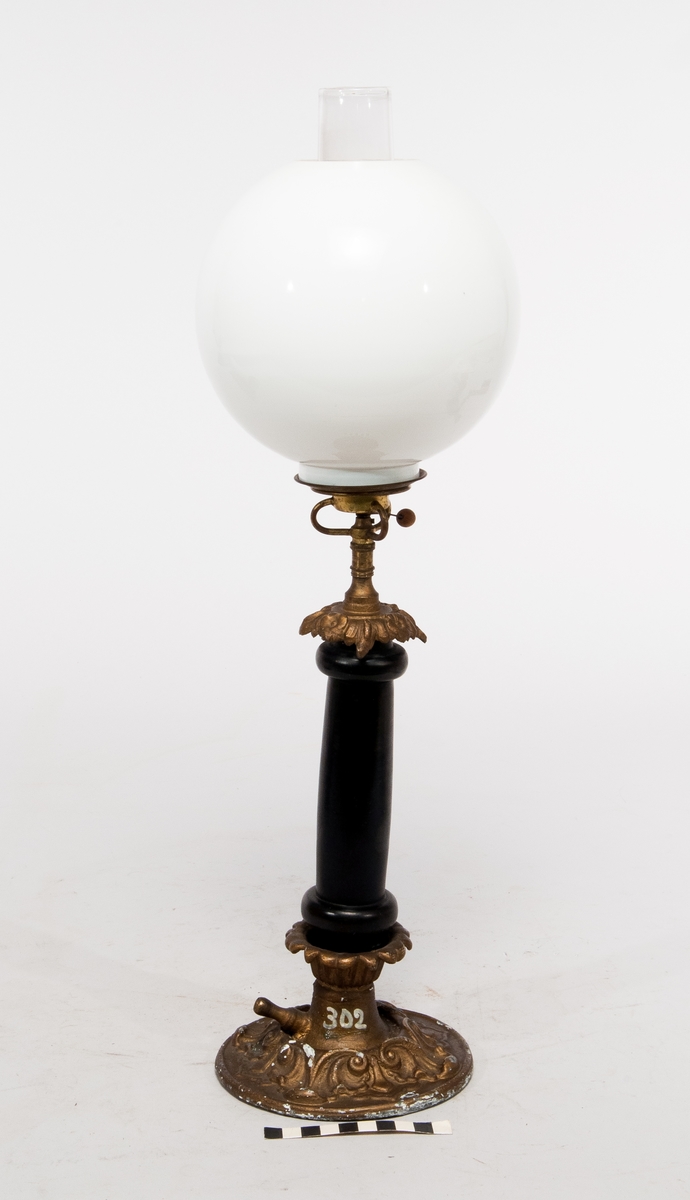 Bordslampa i mässing och trä med en porslinskupa på toppen som täcker glöden från gasen.
Påmålad märkning "302".