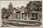 Stationsområde med perrong, växlar och stationshus i bild.