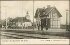 Personal och barn framför station och kyrka vid sekelskiftet.