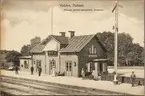 Spårsida av station med personal och resande på perrong.