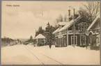 Snötäckt stationsområde med stationshus och vy på bangård.