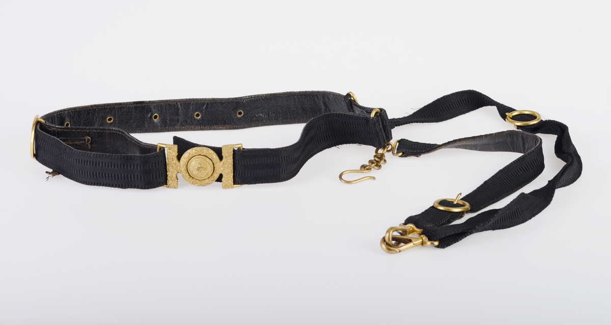 En hatteboks (FTT.56303.01) som inneholder en snutehatt (FTT.56303.02), et bandolær (FTT.56303.03) og en epålett (FTT.56303.04).  
FTT.56303.01:
Hatteboksen er laget av blikk og er svartlakkert utenpå. Lokket er hengslet på baksiden. Oppå lokket er det et enkelt håndtak. I fronetn er det en hempe for hengelås. Den har to lave bein som er laget av sammenrullet blikk. Boksen har form tilpasset hatten. Esken har ikke fôr, men det ligger et papir i bunnen.
FTT.56303.02:
En svart uniformshatt, nærmere bestemt en snutehatt eller en tosnutet hatt. Det er gullbånddekor på hver snute. På den ene siden er det festet en stor kokarde i rødt, hvitt og blått. Over denne er det to flate gullbånd som ender i en spiss. I enden er det en gullfarget metallknapp med et anker med en kongekrone over. Hatten er laget av svart silkefloss med svarte silkebånd langs kanten. Hatten har hvitt silkefôr og svettebånd av brunt lær. På svettebåndet er det festet brune skinnreimer til å feste under haken. På den ene siden er det festet en hvit silkesløyfe. Silkefôret har informasjon om produsent, se "Påført tekst/merker". Det er også bilde av en edderkoppe og et edderkoppnett. Hatten har avstivning ved hjelp av papp. Hatten er håndsydd.
FTT.56303.03:
Et bandolær laget av svart skinn, svart silkestoff og messing. Midjebeltet har en spenne midt foran. Spennen har motiv av et anker med en krone over. På innsiden av beltet er det sydd fast en skinnreim med metallhull til å regulere livvidden. Skulderreimen er festet i midjebeltet med metallringer. Delene til skulderreimen festes sammen med to fjærbelastende kroker. Ved sammenføyningen skulderreim og midjebelte er det påmontert en liten kjetting med krok.
FTT.56303.04:
En skulderklaff til uniform. Oversiden består av svarte- og gullfargede flettede snorer. På undersiden er det sydd på svart ullstoff som er like bred som klaffen. I den ene enden er det sydd på en svart knapp som ullstoffet kan festes i.