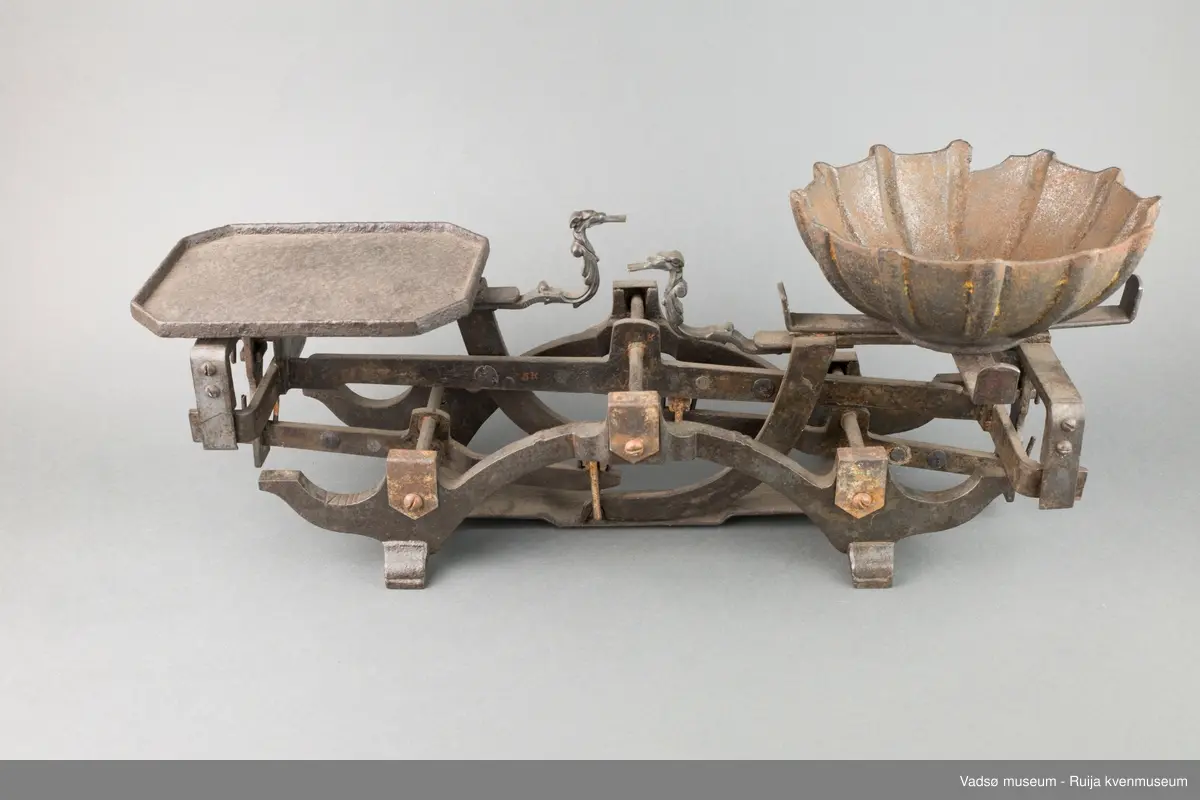 Diskvekt. På ene siden er en rektangulær plate til vektlodd, på andre siden er en løs metallskål for varer. På vektplatene, motstående for hverandre, sitter et ornamentert dyrehode, hver med tunge formet som et flatt jern ut av kjeften. Disse er indikatorer for likevekt. Når "tungene" er i samme høyde og såvidt berører hverandre er vekta i balanse.