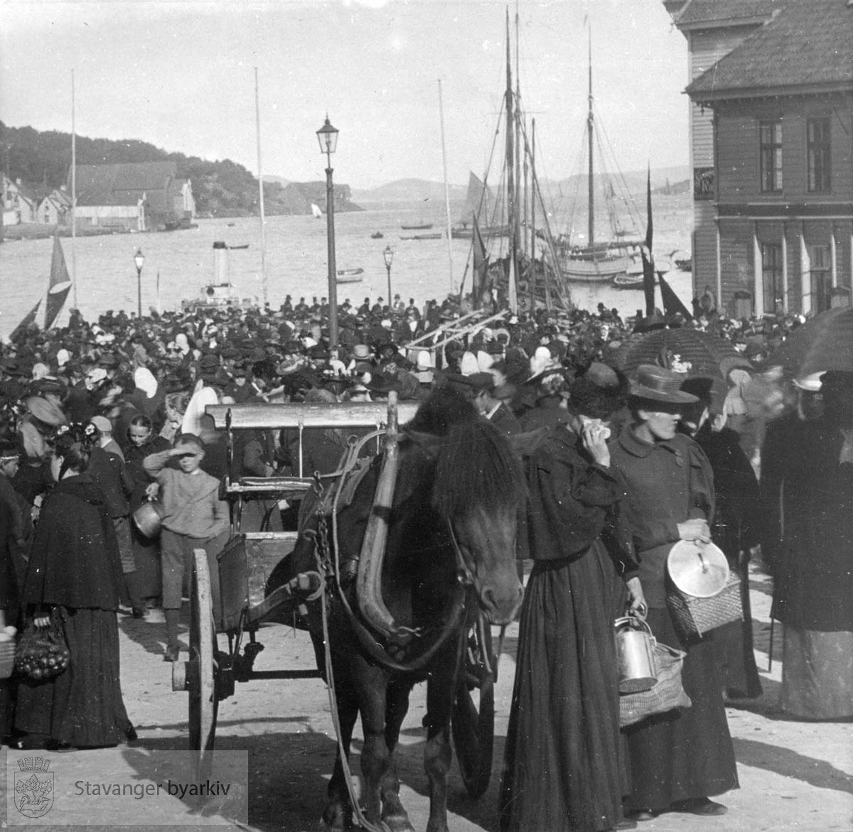 Oversiktsbilde over torget med utsikt utover vågen. Torget er fullt av folk. Utskilt fra PA293. ..Seilbåt.Seilskute.