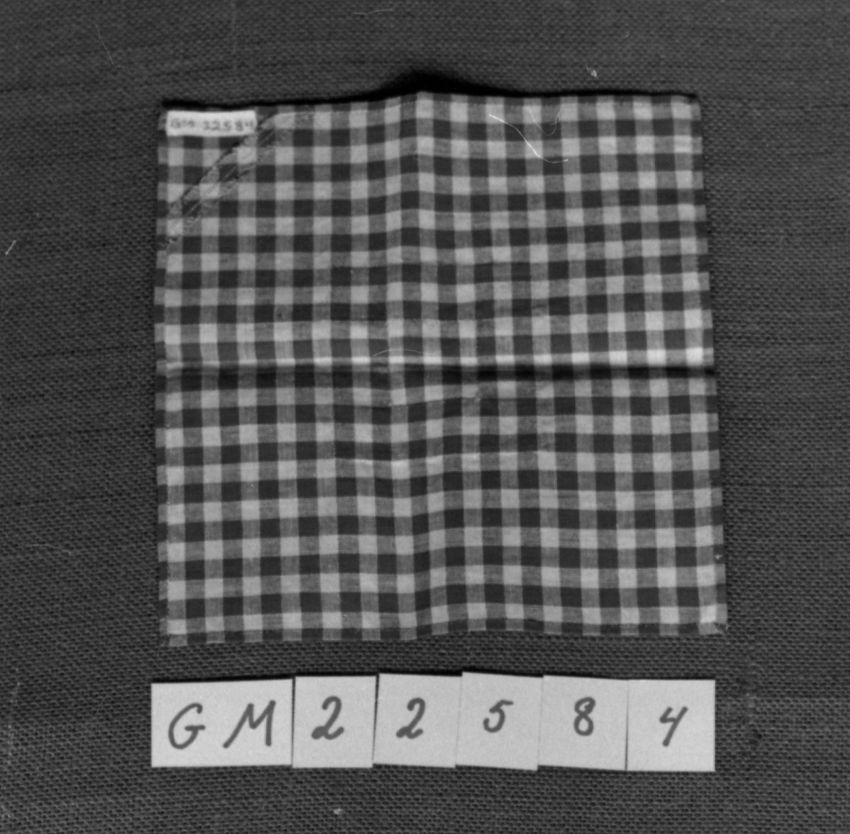 Firkantet tøylapp kantsydd for hånd og med lapp sydd på over hull