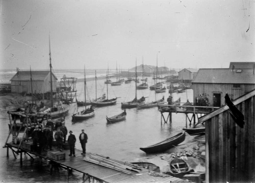 Herøy, Sandsundvær. Sandsundvær ved flo sjø. "Kjilo", sundet mellom holmene, sett fra moloen "Ytterloddet" mot nordøst. Det er ennå ikke kommet rekkverk på moloen. Moloen kom i 1907 og rekkverket i 1913.