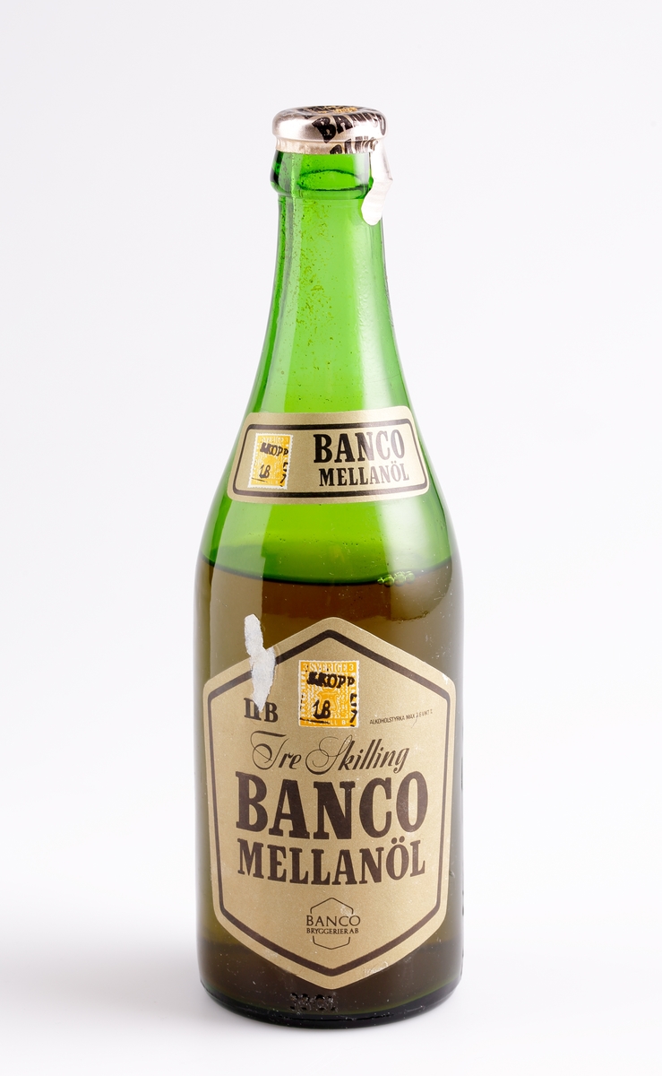Ölflaska med öl. Maskintillverkat. Etikett: överst - "BANCO MELLANÖL", underst - "ll B Alkoholstyrka Max 3,6 vikt%, Tre skilling BANCO MELLANÖL, BANCO bryggerier AB". Märkt i botten H34. Märkt nederst: H29  75  PLM  33 cl. 

Inskrivet i huvudkatalogen efter 1977.