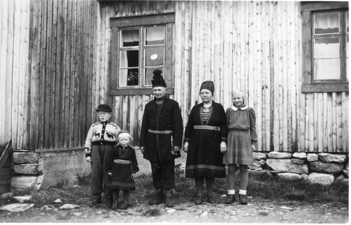 Familieportrett foran bolighus. Foreldre og et av barna i gapta/kofte