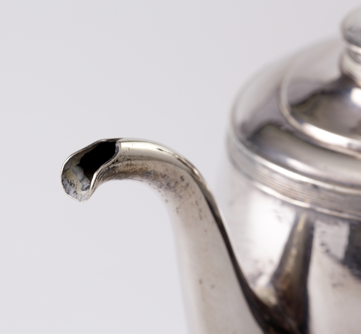 Tekanna av silver. 
Oval modell på fyra tassfötter med palmettdekor. På livet en lejonmaskaron på båda sidor. Välvt lock med gjuten dekor av vinblad och vindruvor. Svarvad, svärtad träknopp. Svärtat uppsvängt handtag av trä. Stämplar på undersidan av kannan.