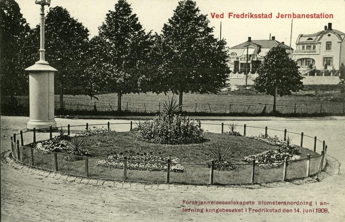 Fredrikstad. Vestsiden. Cicignon. Jernbaneparken (også kalt Stasjonsparken) (i bakgrunnen), anlagt i 1914, tidl. kalt for Schwartzelunden, etter trelastmannen og politikeren Thomas Werner Schwartz (1829-1906) som eide området. - Blomsteranordningen nærmest var anlagt av Forskjønnelsesselskapet i anledning av kongeparets besøk i Fredrikstad 14. juni 1908. - Bygningene i bakgrunnen: Kongens gate 2 (tv) og Welhavens gate 11.