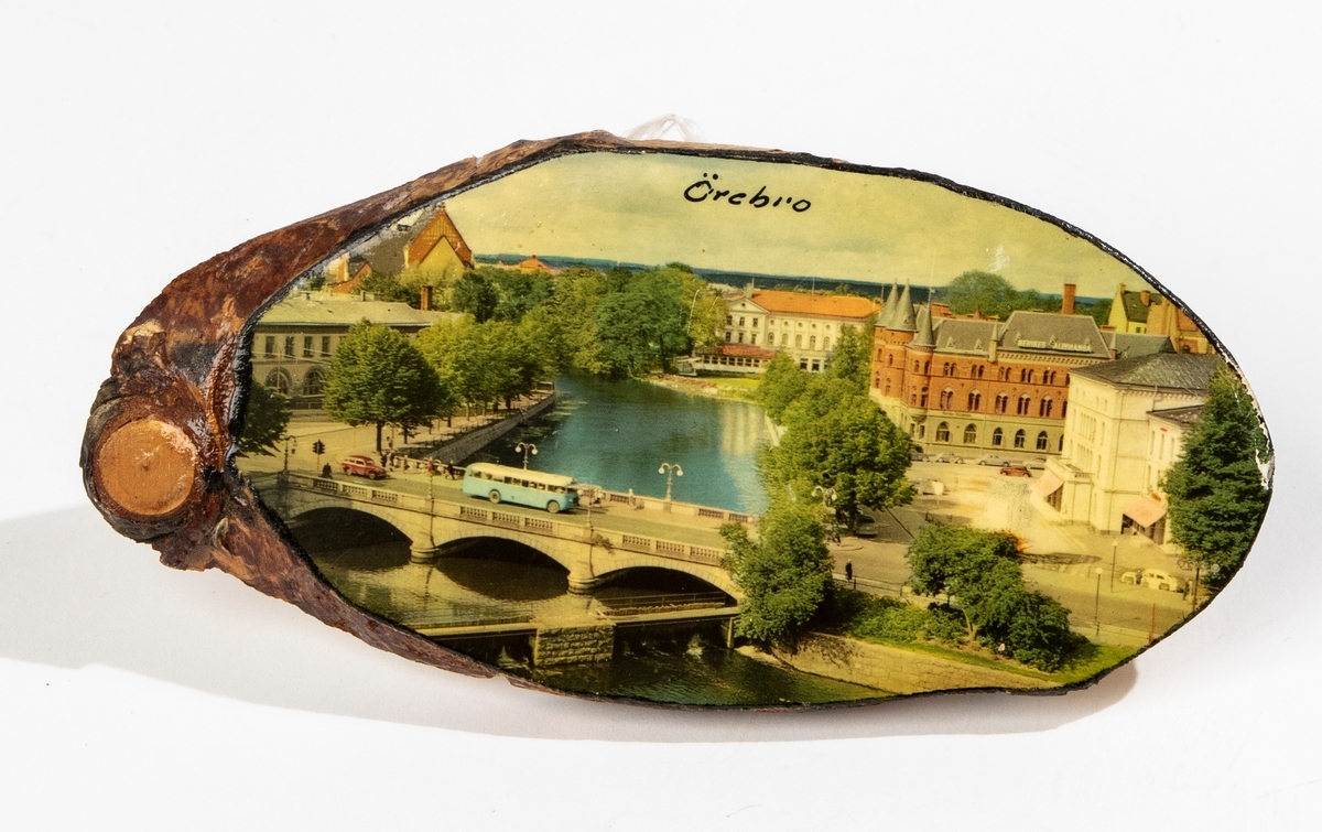 Björktavla, snedsågad björkstam med pålimmat vykort i färg föreställande stadsbild på Örebro, överst text "Örebro". På baksidan upphängningstråd med två häftstift, och prislapp märkt: "10:-".
