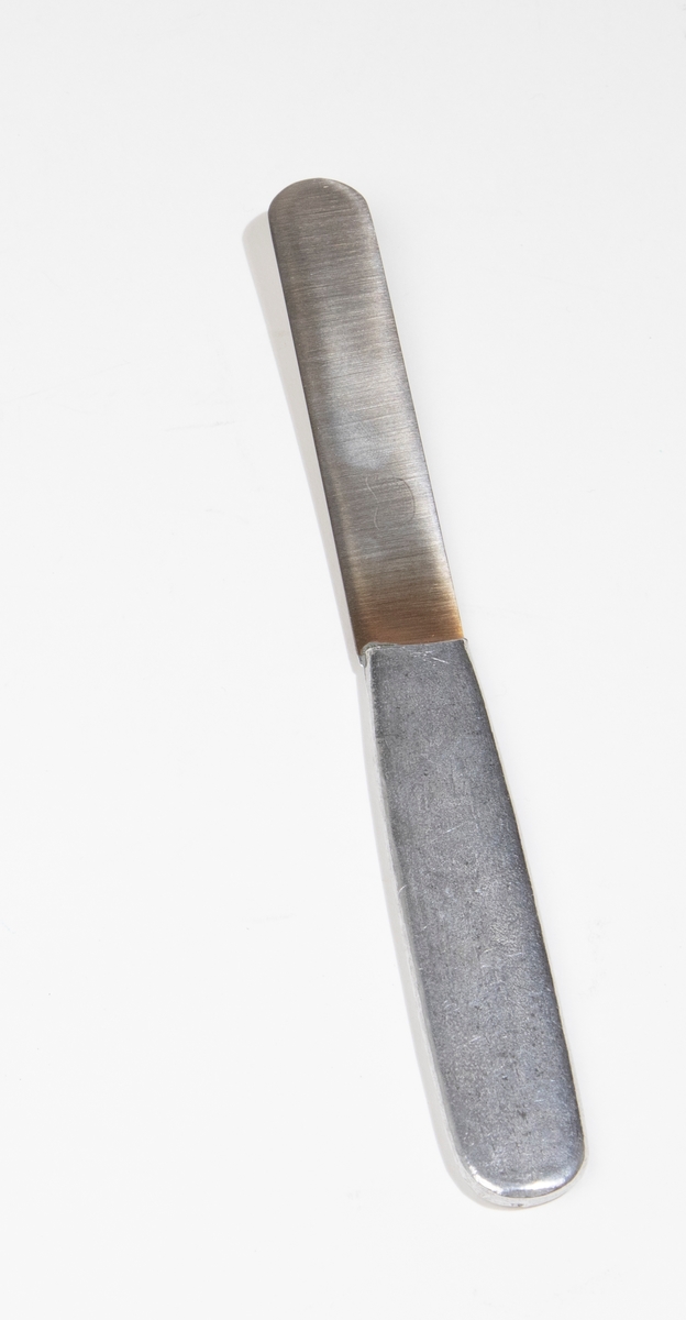 Kniv av lättmetall. Hör ihop med sked (JM 54960:1), gaffel (JM 54960:3) och förpackning (JM 54960:4). Stämplad: "ROSTFRITT STÅL BAS".