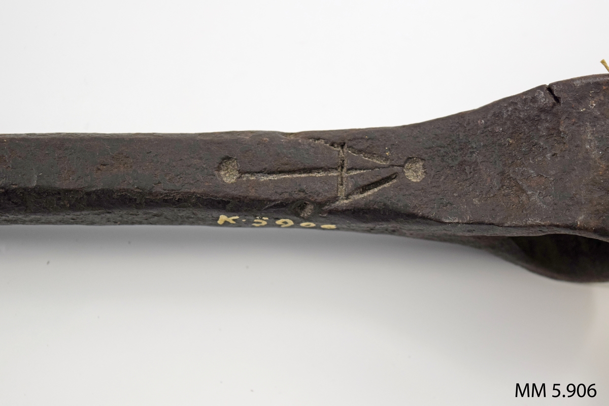 Nedre änden utsmidd till skär. Den övre vriden till ögla för handtag för vridning av borret. 

Märkt med ett uppochner vänt V med ett streck igenom.