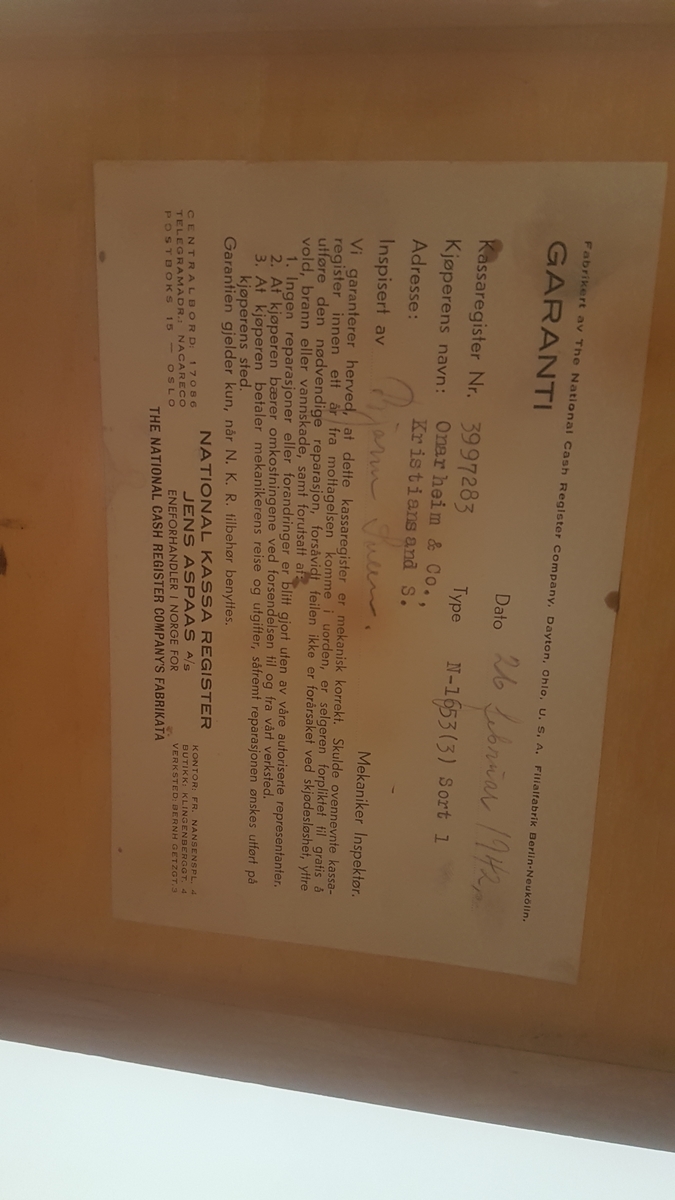 Kassa-apparat med sokkel, pengeskuff og sveiv, 5 skalaer for kr. og øre. Vindauga for kronesum framme og bak. 5 knottar. Nøkkel til skuff.