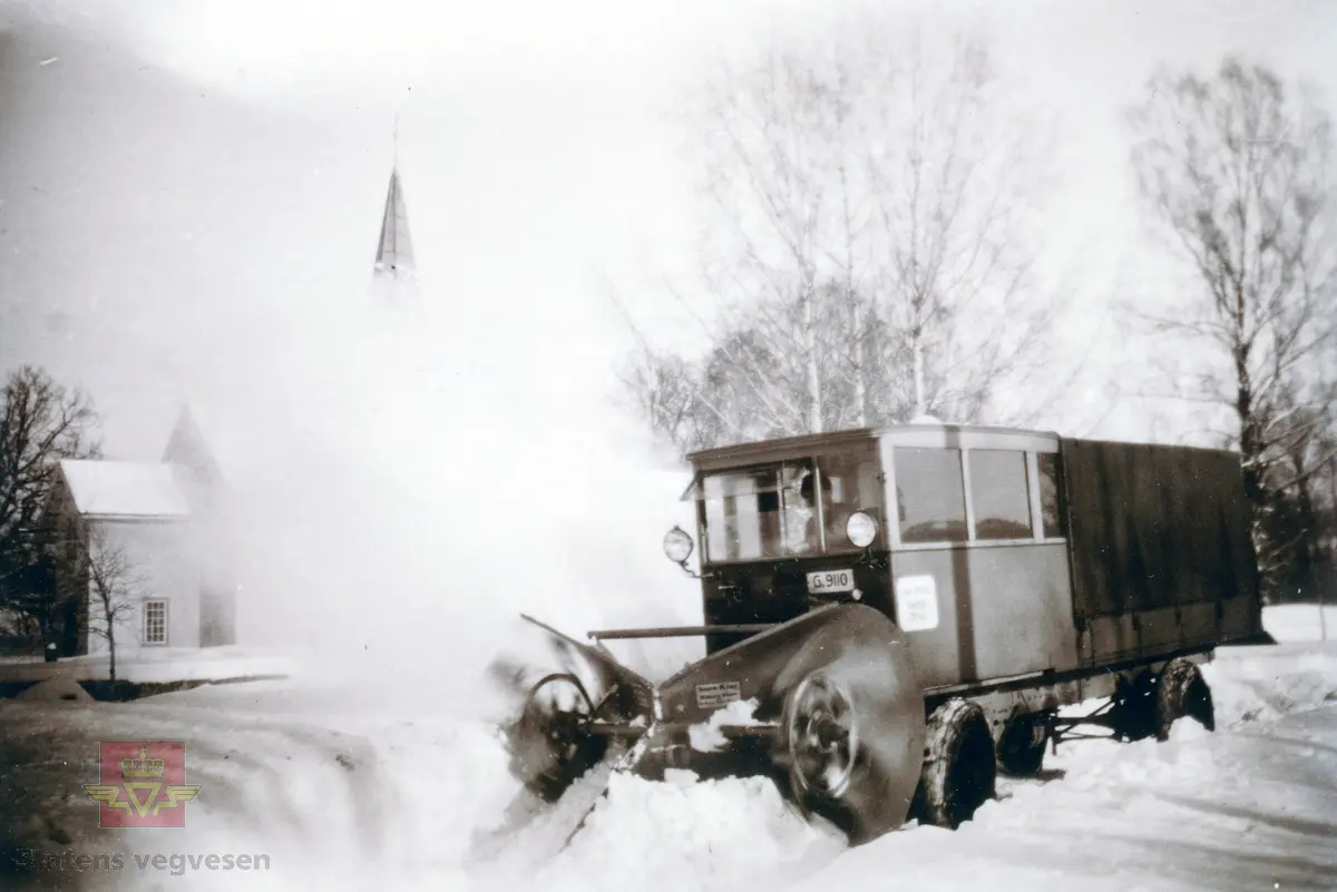 Snøbrøyting. Utprøving av ulike typer snøfresere eller roterende snøploger, vinteren 1928. Her en fres av typen "Snow King" importert av firmaet Colbjørnsen & Co A/S, Utprøvd i Lågendalen med økonomisk støtte fra  Vegvesenet. Her montert på en FWD lastebil (G-9110) som brøyter på Lågaveien foran Svarstad kirke.