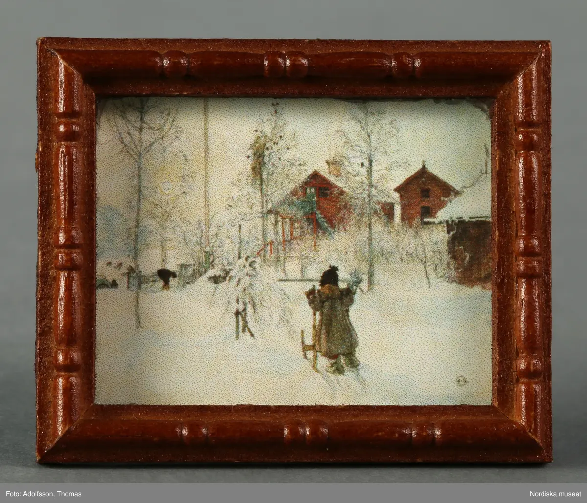 Tre inramade tavlor som hör till flickrummet på översta våningen i dockskåpet. En föreställer, a), "Gården och brygghuset" av Carl Larsson i miniatyr och de andra två ,b-c), är porträtt av okända personer.