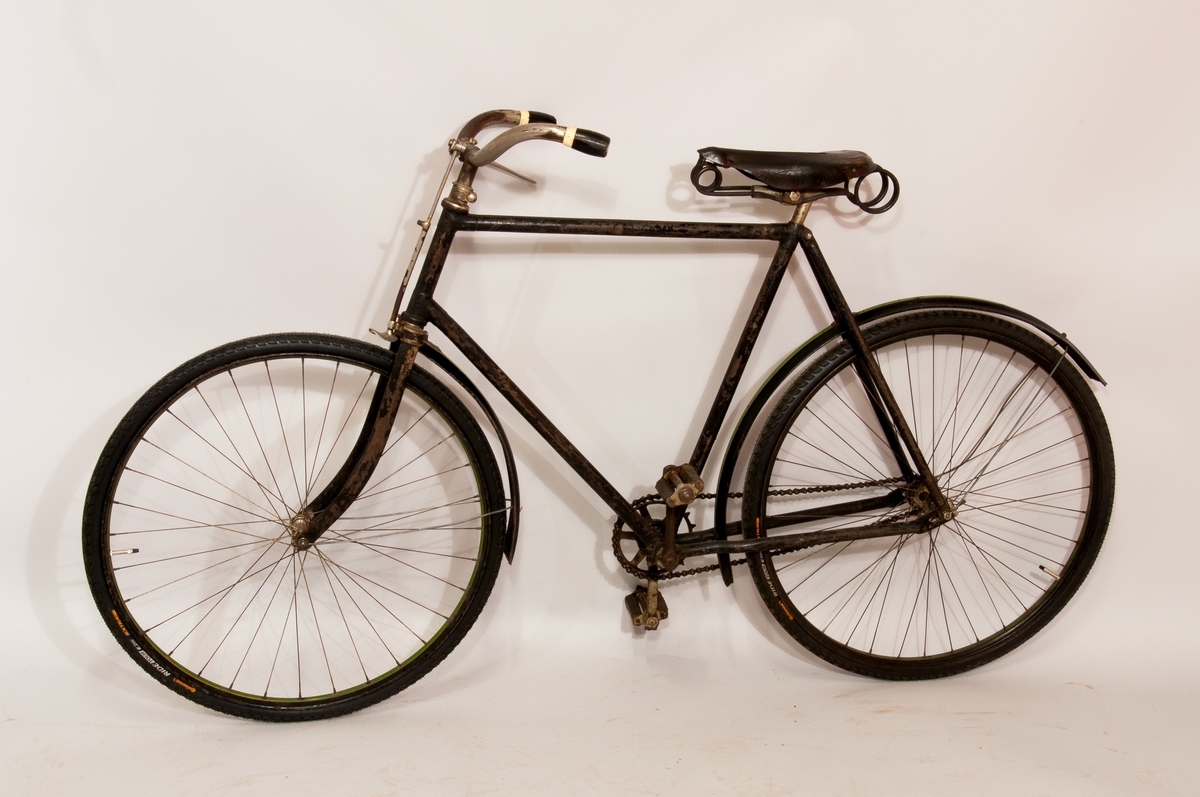 Tvåhjulig cykel med luftringar och fast kedjedrift på bakhjulet. Ram av stålrör med skärmar av plåt och fjädersadel klädd i läder. Ringklocka på styret. Svart med gröna ränder på skärm. Höger pedalvev och kedjekrans utbytta liksom skärmar och fälgar.