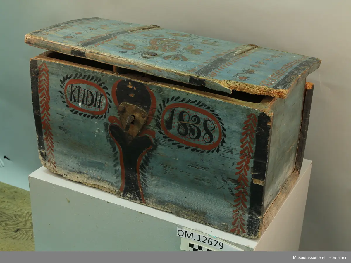 Blå rosemåla trekiste. Loket er hengsla. "KHDH 1838" er måla på framsida. Lås med nøkkel på framsida. Kista er i dårlig stand.