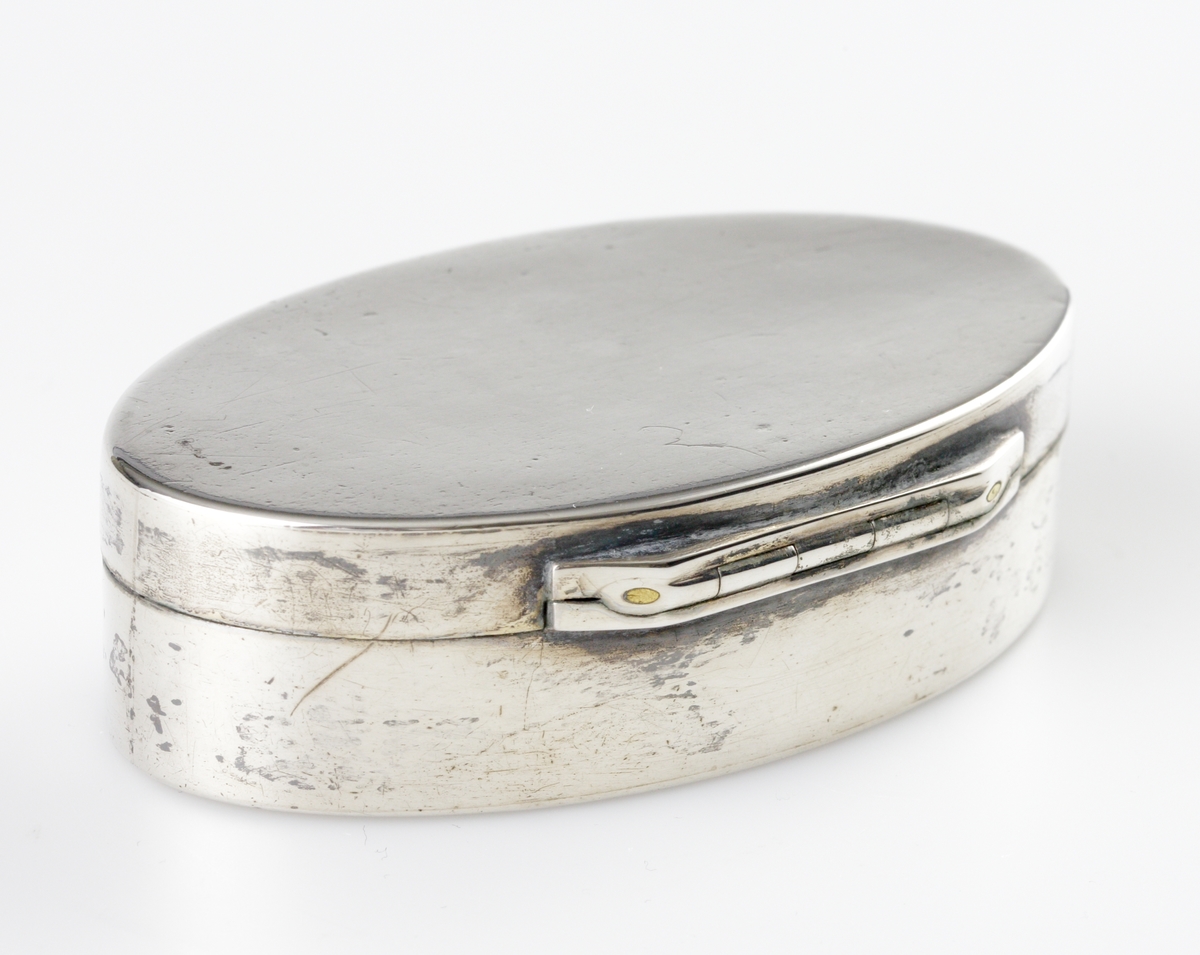 Dosa, silver.
Oval, slät modell. Invändigt förgylld. Ägarinitialer: "J.O.D." på dosans undersida. 
Stämplar (något otydliga) på lockets undersida.