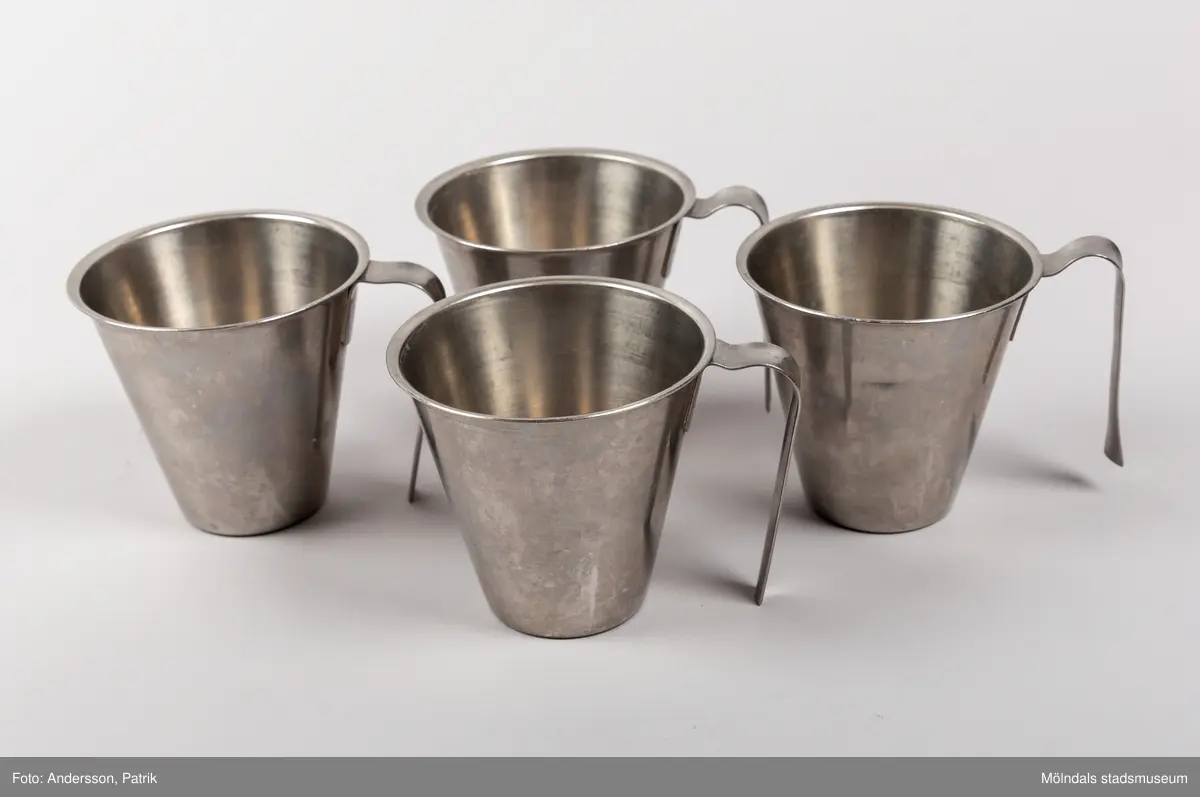 Silverfärgad mjölkbägare med handtag. Tillverkad av rostfritt stål  i Sverige. Bägaren rymmer 3,5 deciliter.