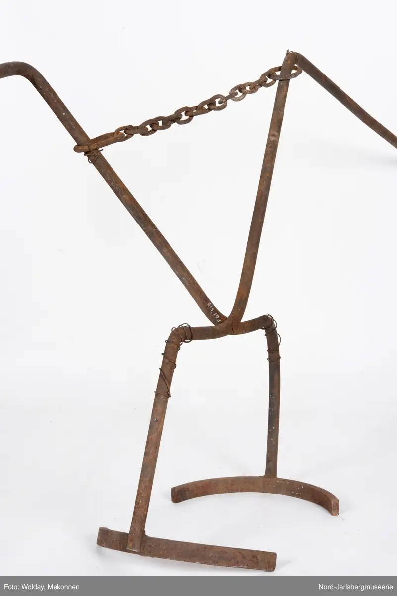 To stenger festet sammen med eb bolt - og en kjetting i mellom,. Stengene er bøyd i vinkler og sveiset  90o  vinkel på en halvbuet stang. Ført sammen vil de omfavne en rund digel.