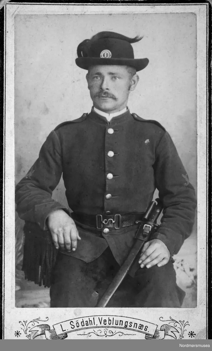 Soldat. Permuniform. Portrettfoto av en ukjent mann i uniform og sverd. Muligens fra Veblungsnes i Rauma kommune. Fotoalbum som stammer fra Marie Opdal (f. april 1894 - d. februar 1981/82), gitt i gave av Torbjørg og Arild Karijord. Fra Nordmøre museums fotosamlinger.