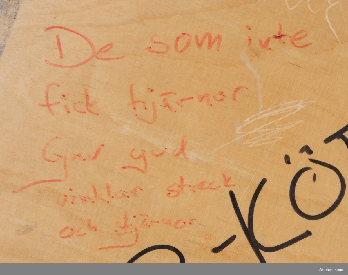 Sängbotten i trä avsedd för våningssäng i metall. Nedklottrad med text och bilder av mestadels sexistisk karaktär. Flertalet kommentarer berör muck och värnpliktens vardag i övrigt. En klisterlapp med Sjöfartsverkets tio sjövettsregler, liksom fem mindre klisterlappar från snusdosor av märkena Göteborgs rapé och General är fastsatta.