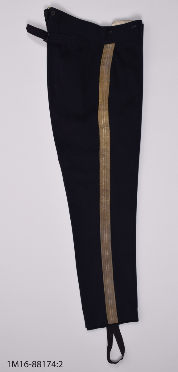 Uniformsbyxa, till lantmäteriuniform för kommisionslantmätare, av mörkblått kläde med guldrevärer längst sidorna. Sprund baktill i midjehöjd, med hank för upphängning av byxorna. Nio mörkblå knappar längs midjan. Gylften knäpps  med sex mörkblå knappar samt en hake och hyska. Fodrade upptill med beiget sidentyg med grå ränder. En ficka på vardera sida, med fickpåsar av beige bommullssatäng. Baktill byxspänne fodrat med grovt linnetyg. Nedtill på byxbenen hälla för foten, en saknas.