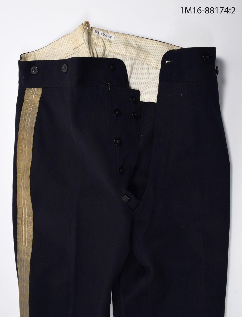 Uniformsbyxa, till lantmäteriuniform för kommisionslantmätare, av mörkblått kläde med guldrevärer längst sidorna. Sprund baktill i midjehöjd, med hank för upphängning av byxorna. Nio mörkblå knappar längs midjan. Gylften knäpps  med sex mörkblå knappar samt en hake och hyska. Fodrade upptill med beiget sidentyg med grå ränder. En ficka på vardera sida, med fickpåsar av beige bommullssatäng. Baktill byxspänne fodrat med grovt linnetyg. Nedtill på byxbenen hälla för foten, en saknas.