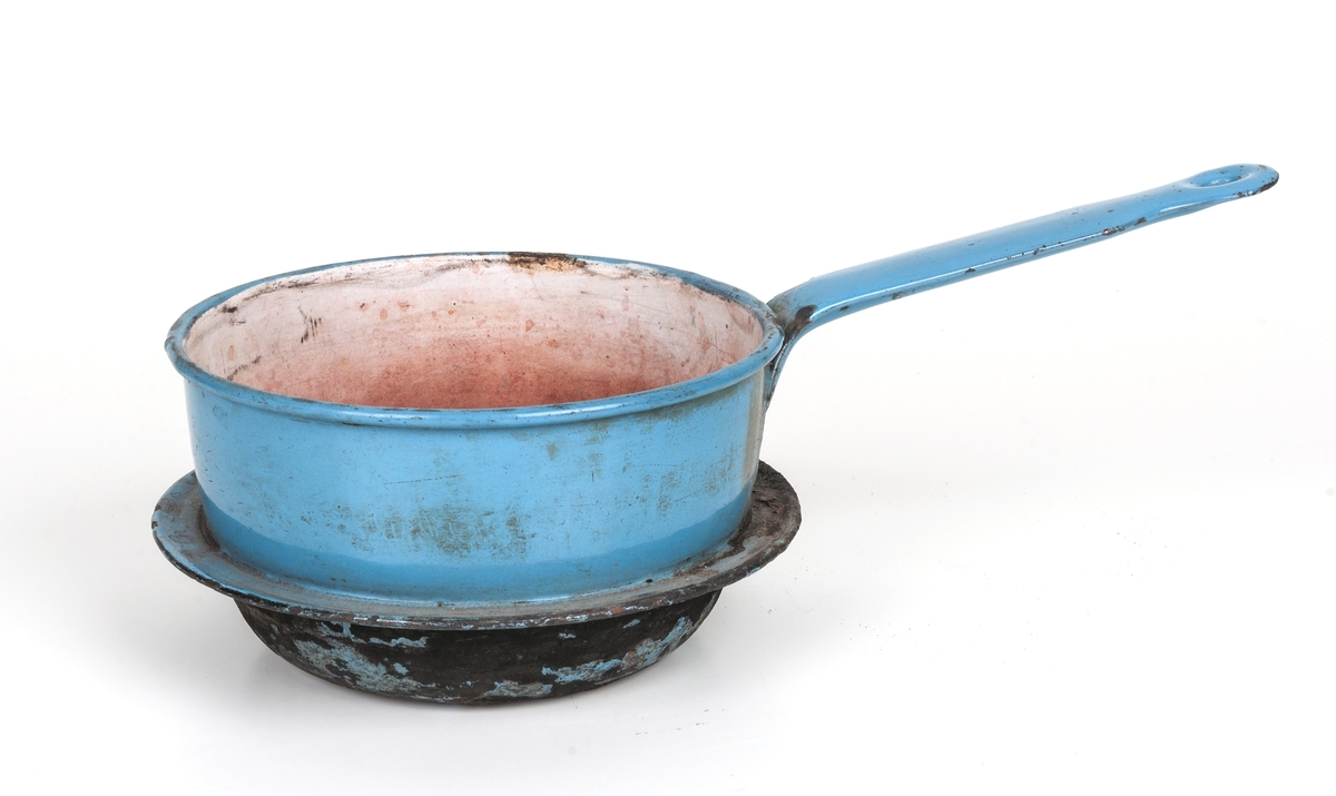 Kastrull, emaljerad med fotring för användning i vedspis.
Blå. Rundad botten. Diam 15cm, skaftlängd 14,5cm, höjd 8,5cm. Sotig botten.