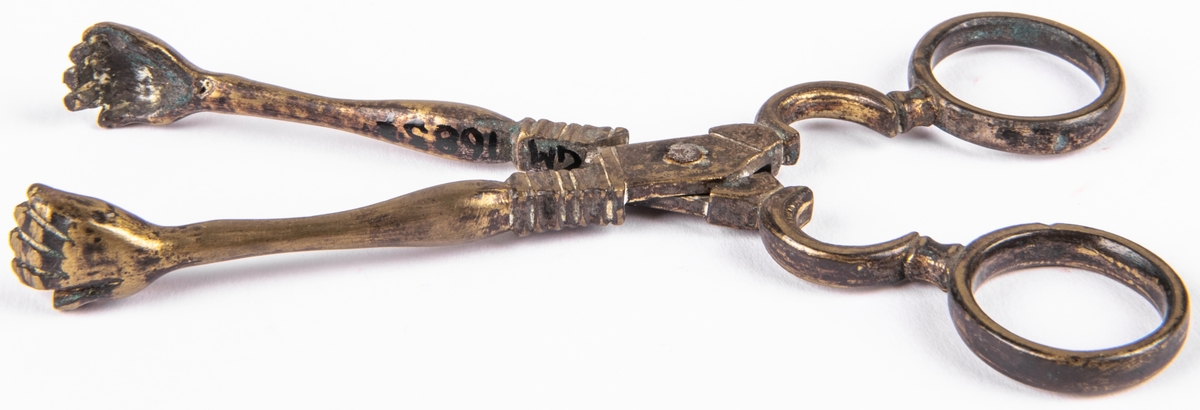 Sockertång, mässing. Sockertångsarmarna avslutas med ett par händer.