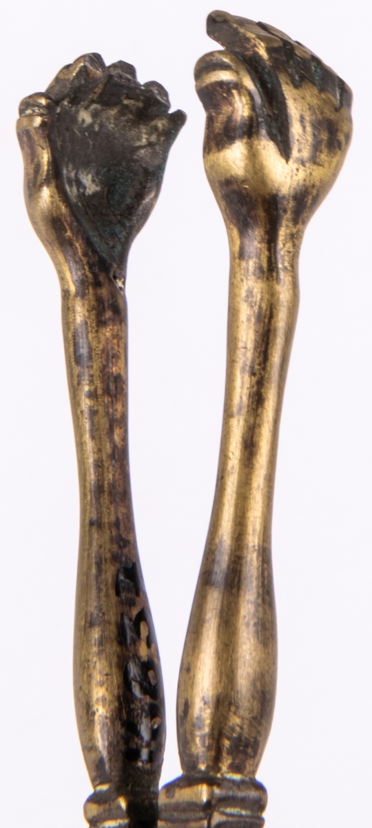 Sockertång, mässing. Sockertångsarmarna avslutas med ett par händer.