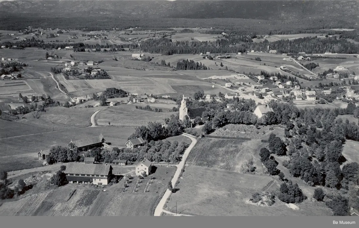 Flyfoto av Bøhaugen med kyrkjene og Midt-Bø gardane, tatt 5. juli 1952.