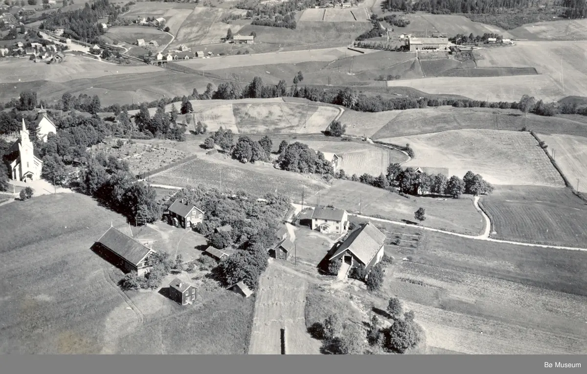 Flyfoto av Bøhaugen med kyrkjene og Midt-Bø gardane, tatt 5. juli 1952.