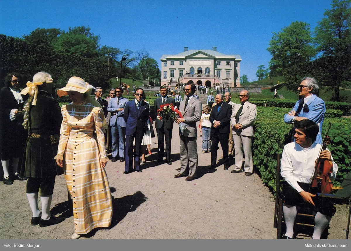 Kungabesök på Gunnebo slott, år 1977. I mitten ses Kung Carl  XVI Gustaf hållandes en  blombukett. Längst till vänster Jan Ivar Blixt. Till vänster om kungen står rektor Åke Baaz och landshövdingen Erik Huss. Längst åt höger står fil.dr. Nils Dahlbeck och chefrededaktör Jon E. Lisshammar. mannen som sitter på en stol längst ut till höger är Ivan Hagberg.
Vykort, förlag: Mölndals Kommun.