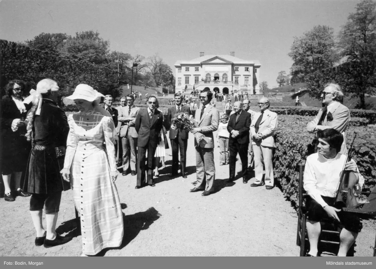 Kungabesök på Gunnebo slott, år 1977. I mitten ses Kung Carl  XVI Gustaf hållandes en  blombukett. Längst till vänster Jan Ivar Blixt. Till vänster om kungen står rektor Åke Baaz och landshövdingen Erik Huss. Längst åt höger står fil.dr. Nils Dahlbeck och chefrededaktör Jon E. Lisshammar. mannen som sitter på en stol längst ut till höger är Ivan Hagberg.
Vykort, förlag: Mölndals Kommun.