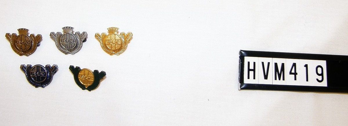 Cirkelrund nål med "granbarr" runt om. Finns i brons, silver, guld, blå, guld med gröna barr.