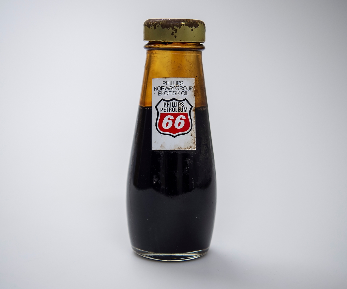 Oljeprøve fra Ekofisk oppbevart i en flaske med skrukork. På ene siden er merkelapp med Phillips Petroleums logo. På den andre siden er merkelapp med Offshore North Sea (ONS) 1974.