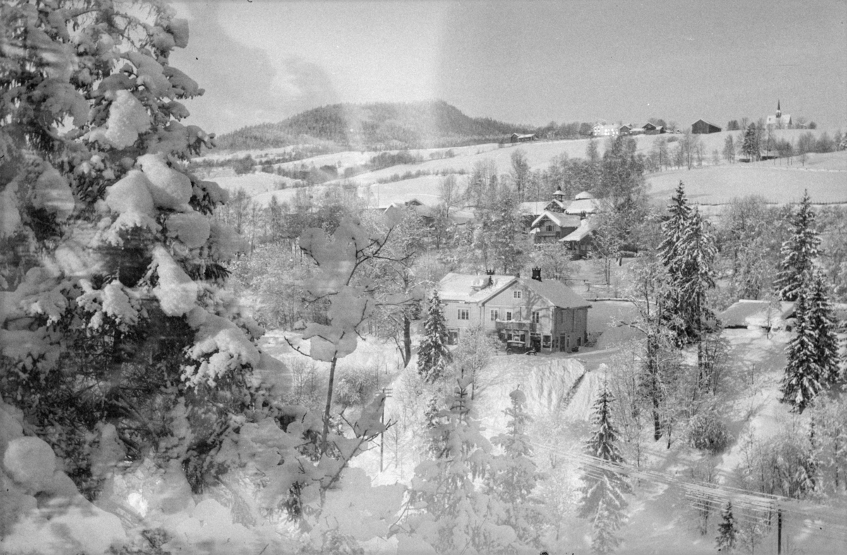Gausdal, Follebu med Tørudstad Landhandleri i forgrunnen. Bak synes deler av Aulestad og Follebu kirke i bakgrunnen. Mann som måker snø av taket på butikken. Vintermotiv